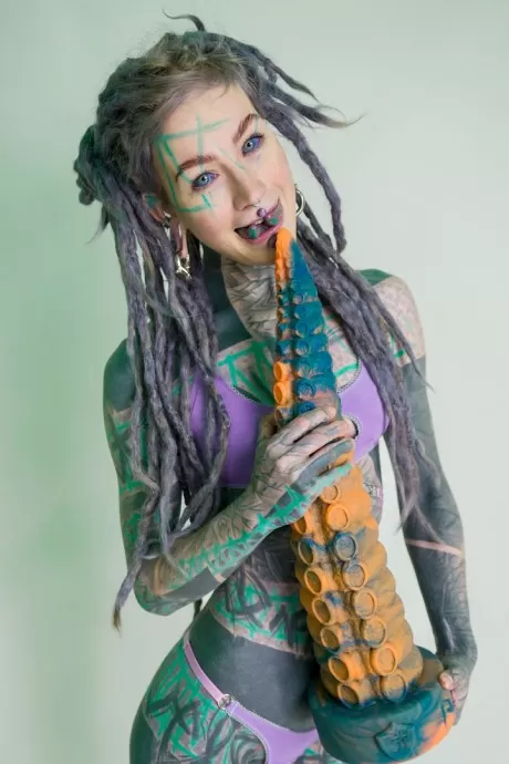 Сильно татуированная девушка Anuskatzz держит пару игрушек для порчи в обнаженном виде