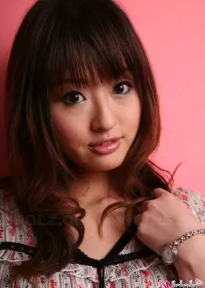 Японская модель с симпатичным личиком стоит одетая на фоне розовой стены