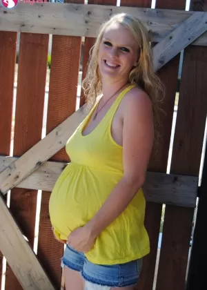 Pregnant blonde amateur Kristi shows her swollen tits and belly by a gate